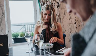 a man and woman sit at a table, eating food and drinking wine with a view from the elephant rock hotel
