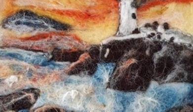 a felted landscape depicting a lighthouse on the rocks with an orange sky