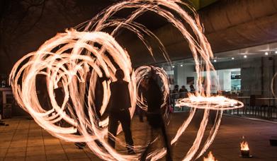 people spinning wheels of fire in the darkness in a square