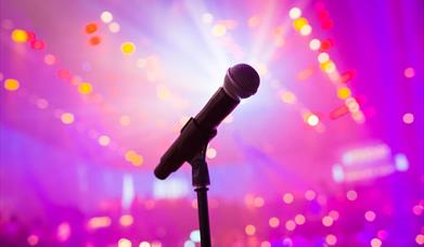 Microphone on a stand against a pink backdrop illuminated with lights