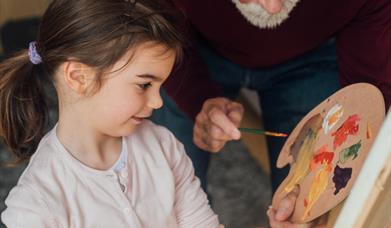 a grandparent and a child painting on a canvas at an easel with an art palette