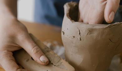 a person's hands sculpt a container made from clay