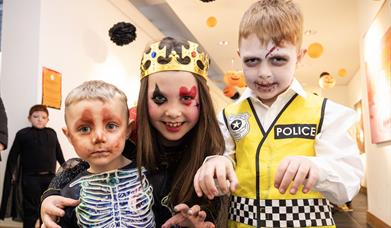 iamge of 3 children in fancy dress as a skeleton, a zombie police officer and the queen of hearts
