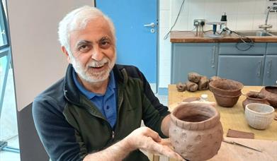 a man proudly presents a hand sculpted pot