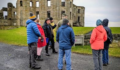 Bob Picken guiding a group in outdoor clothing while looking at the ruins on the Downhill Demesne