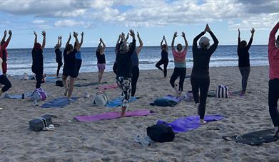 a group of people doing yoga stretches on a beach 