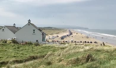 A view over Portstewart Strand in the busy summer season with cars parked all along the beach and families enjoying their day out.