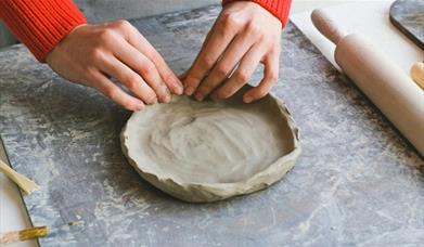 a person working on a shallow clay dish
