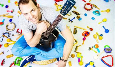 kyle riley surrounded by children's instruments, holding a guitar