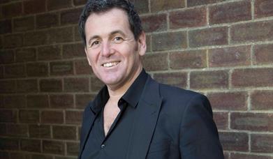 Singer Mike Sterling standing against a white wall wearing a black suit
