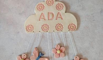 A ceramic cloud with various hanging flowers. The name "Ada" is engraved on the cloud.