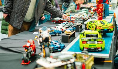 people examining various tables and rows of lego sculptures