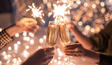 Wine glasses clink together in front of sparklers on New Year's Eve