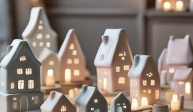 a collection of small ceramic Nordic-style houses illuminated with lights sit on a wooden surface