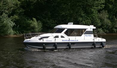 image of cruise boat in water with river bank and tress in the background.