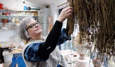 Patricia reaches for dried grass in her workshop