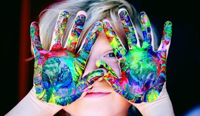 a child peaks through hands that are covered in paint