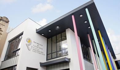 Outside view of the Roe Valley Arts & Cultural Centre - a white building with large windows and bright pastel coloured pillars at the side