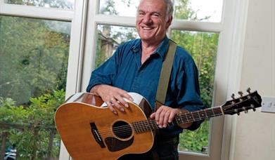 Image of a man in a blue shirt holding a guitar with a strap