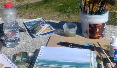 art supplies all gathered on an outdoor table with grass in the background