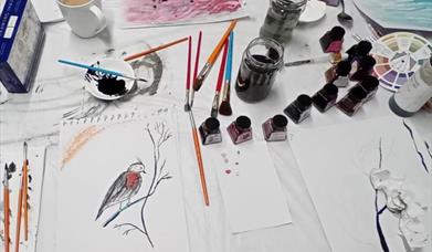 a variety of brushes and inkpots next to a painting of a small bird on a branch