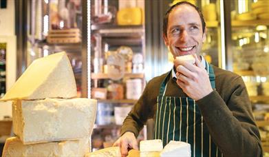 Kevin Sheridan in a striped apron, smiles while tasting cheese