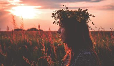 a woman with a floral crown standing against a summer sunset