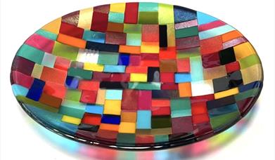 A shallow glass dish made from various different colours arranged in geometric patterns. 