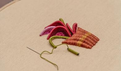 close up of a stumpwork embroidery piece with a needle stuck int he embroidery hoop canvas