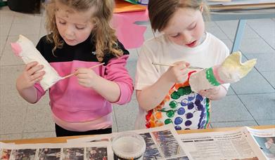 two children are painting papier-mache creations