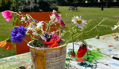 A bundle of colourful flowers potted in a makeshift planter, with a park and clear blue sky visible in the background.