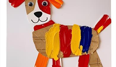 A crafted puppy make of various pieces of cardboard and other materials, painted with a range of colours.