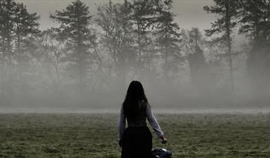 Image  showing a girl holding a bucket standing with her back to the camera, in a misty field