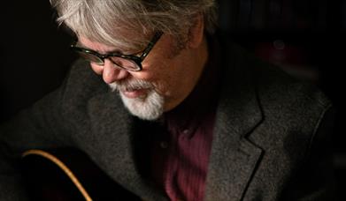 musician Anthony Toner looks down towards an acoustic guitar