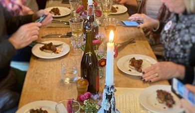 people are eating at a large wooden table by candlelight