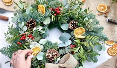 person's hand adds dried oranges to a festive christmas wreath