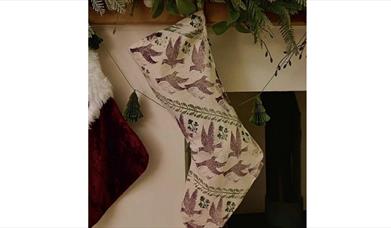 a linen christmas stocking which has been designed with ink printing hangs from a mantlepiece draped with a festive garland