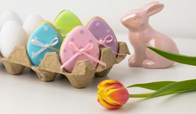 a porcelain rabbit statue sits next to an egg box containing ceramic egg decorations 