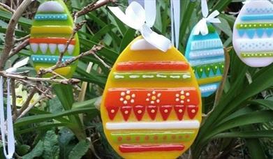 glass easter eggs  layered with coloured glass shapes and powders hanging on a plant
