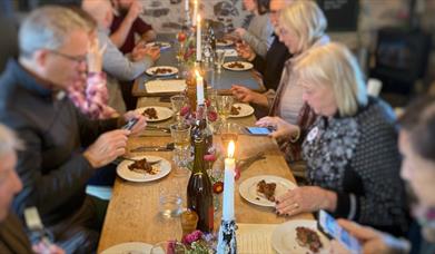 People sitting either side of a long wooden table decorated with candles and wine bottles. 