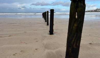 a picture of a beach with wooden posts buried in the sand, forming a line that leads to the horizon