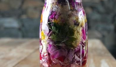 Image shows a close up of a jar filled with liquid and colourful herbs.