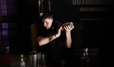 Man holding a cocktail shaker in a dimly lit bar setting