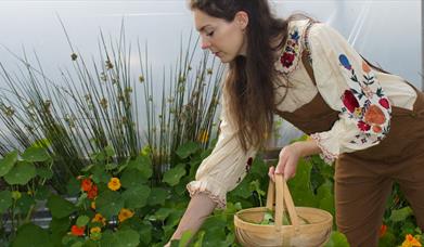a person holds a wicker basket while reaching for plants
