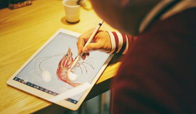 close up of an ipad with person's hands using a digital pen to draw a shrimp