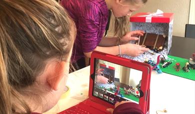 Children taking pictures of a small set using lego figures, to be animated in stop motion. 