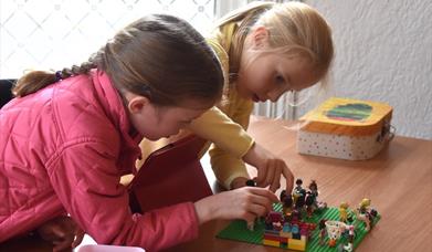 Image shows two young girls building a scene from Lego