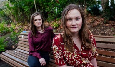 Laura Quirke and Claire Kinsella of the band Lemoncello sitting on a bench together