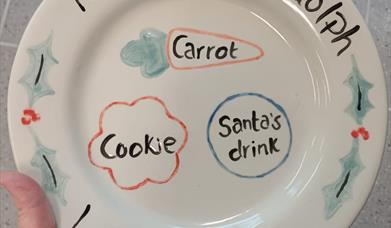 a dinner plate with hand painted spaces for santa's drink and cookie and a carrot for his reindeer.
