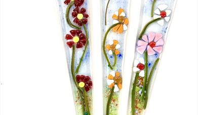 Image shows three glass stakes with flowers in bright colours
